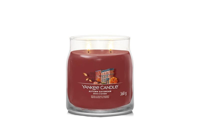 Candela profumata in vaso. Cera rossa, contenitore in vetro trasparente. Scritta: Yankee Candle, Autumn Daydream, 368 g. Due stoppini.