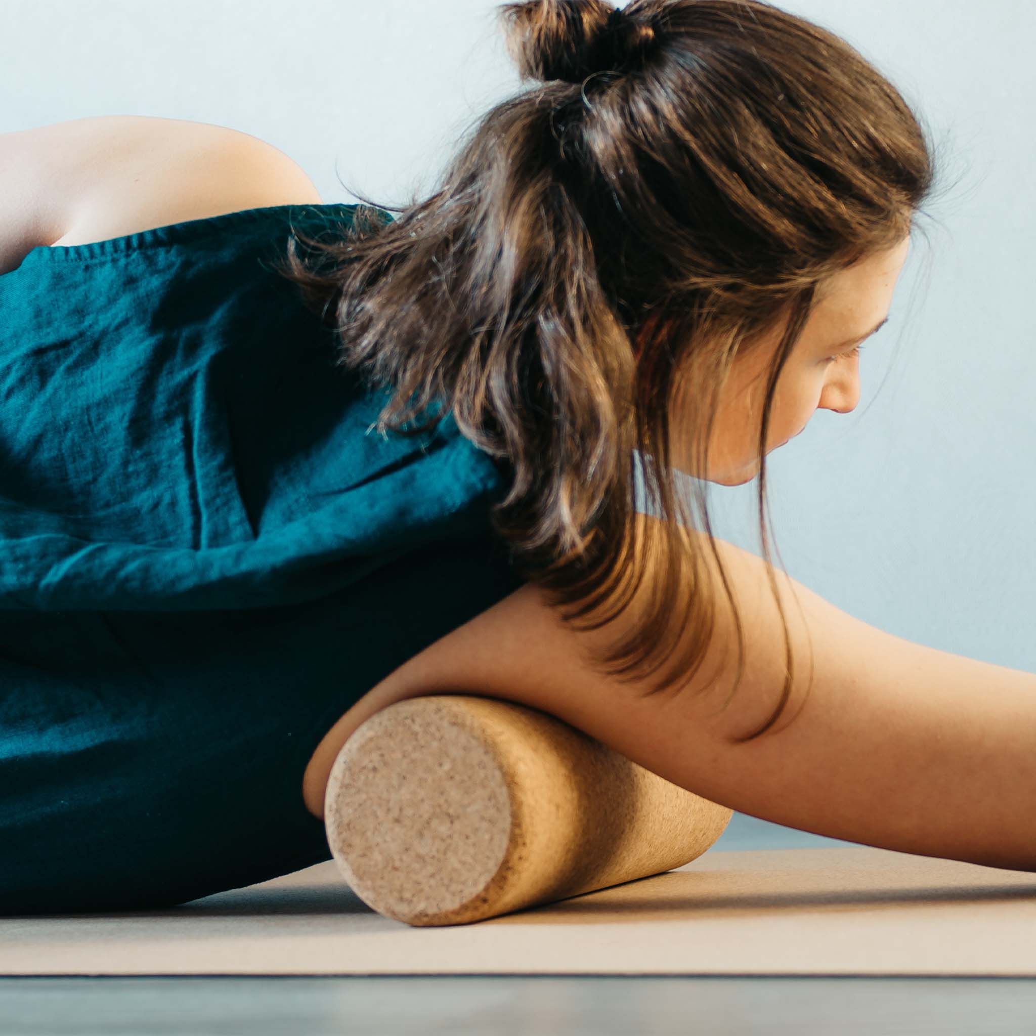 Persona che usa un rullo per fascia in sughero. Rullo marrone sotto il braccio su un tappetino.