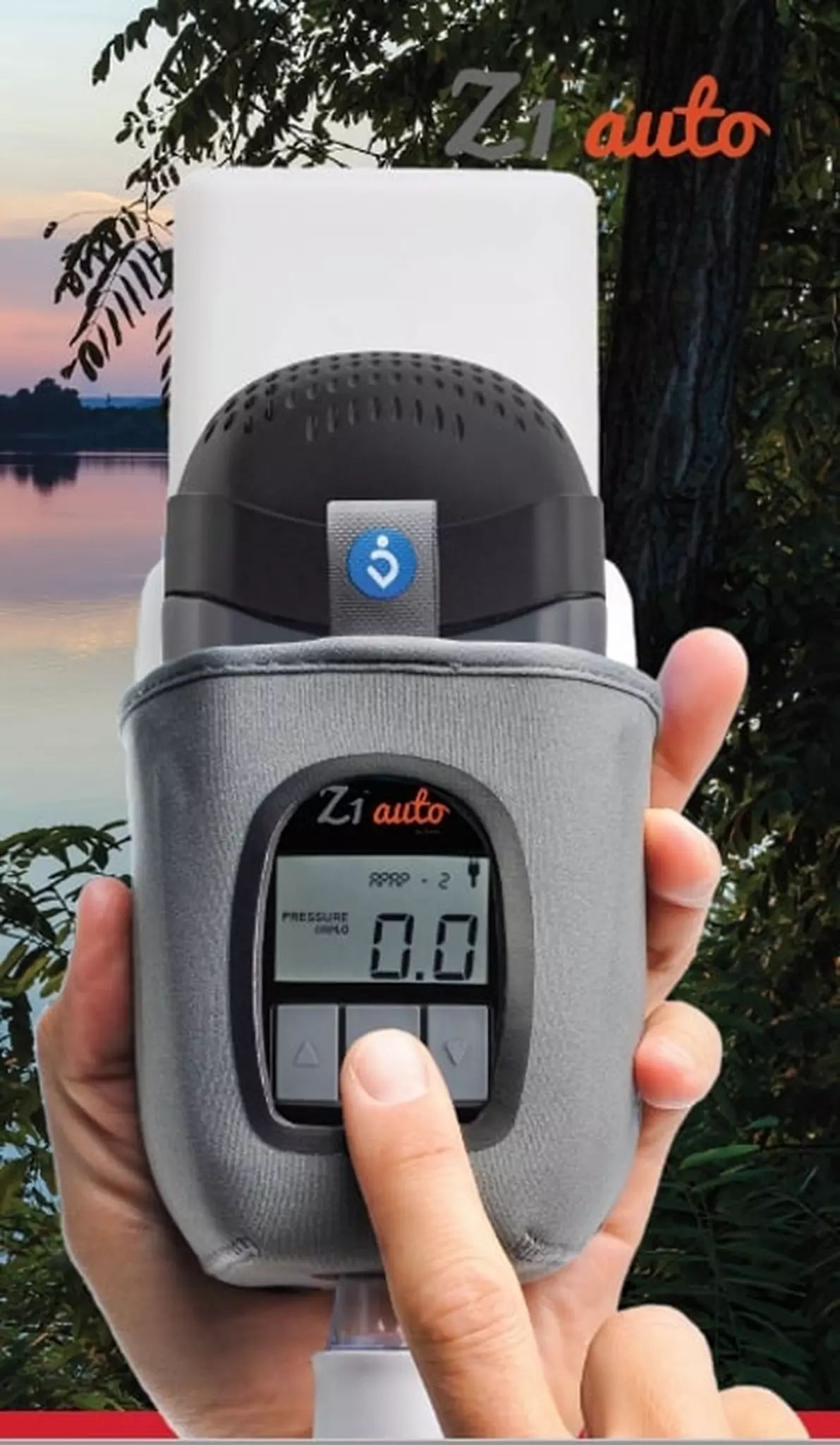 Dispositivo CPAP da viaggio grigio con display, tenuto da mani, davanti a lago e alberi.