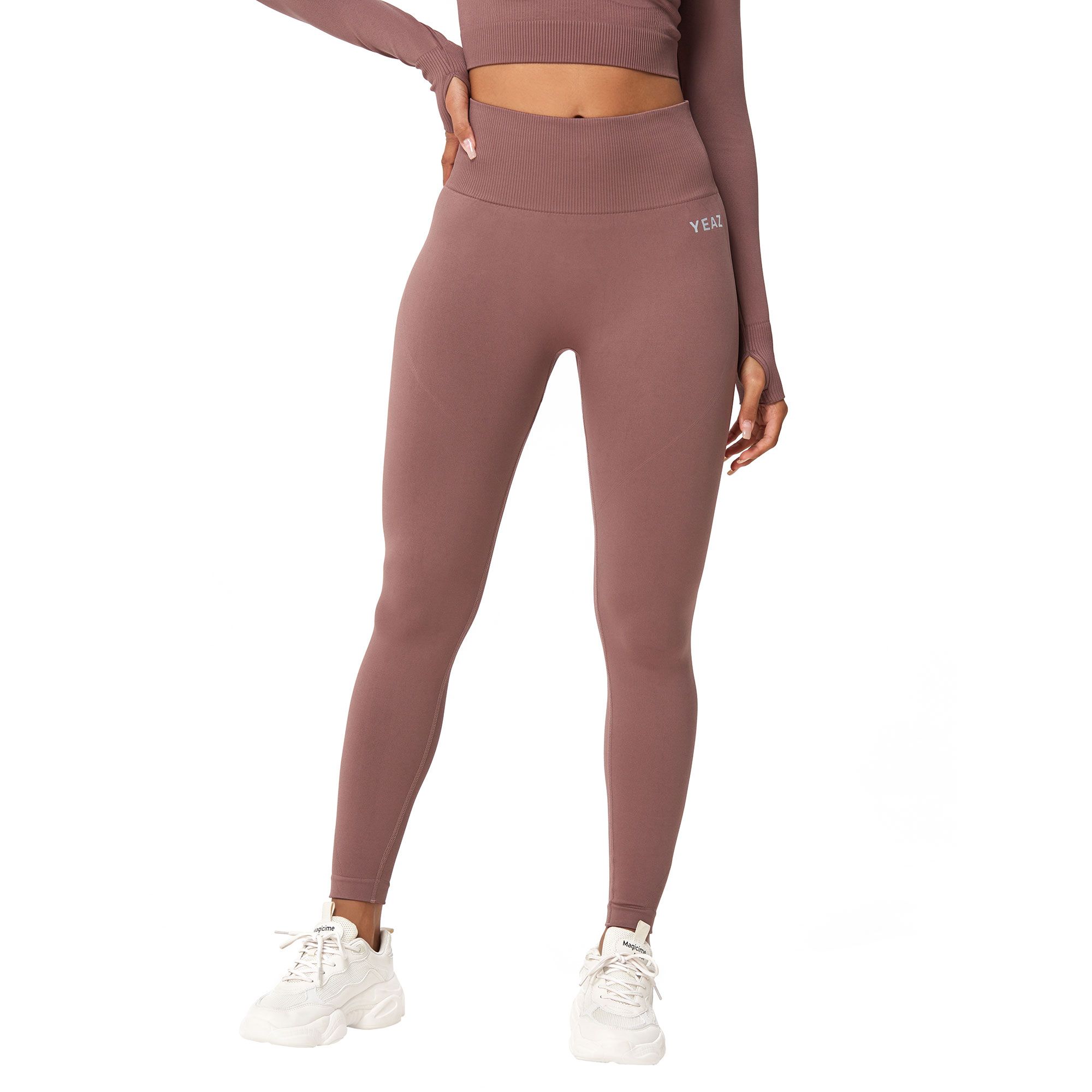 Leggings senza cuciture marroni con logo bianco sul fianco sinistro e fori per i pollici sulla parte superiore.