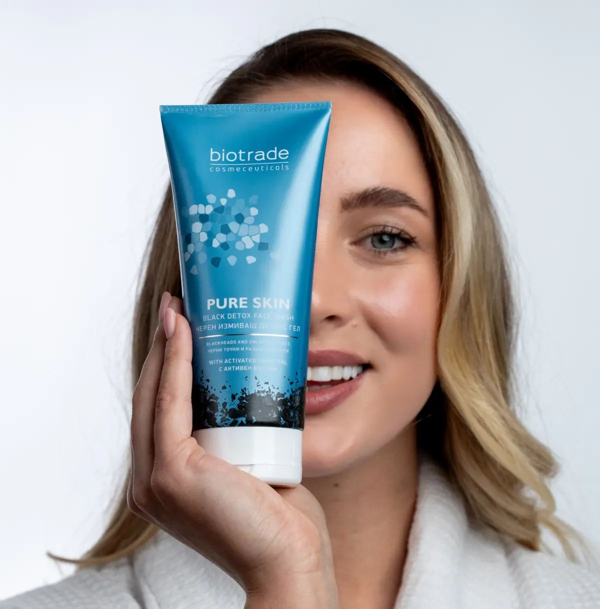 Donna tiene un tubo blu-grigio davanti al viso. Scritta: Biotrade, Pure Skin Black Detox Face Wash.
