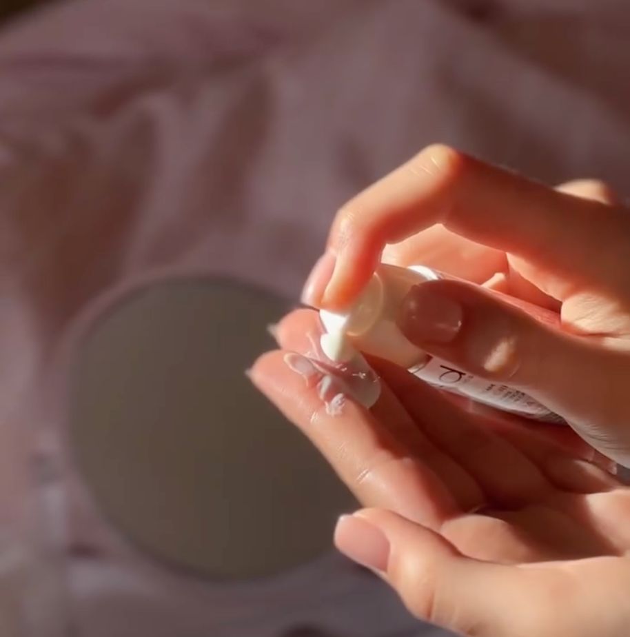 Crema solare erogata da un flacone bianco con dosatore sulla mano.