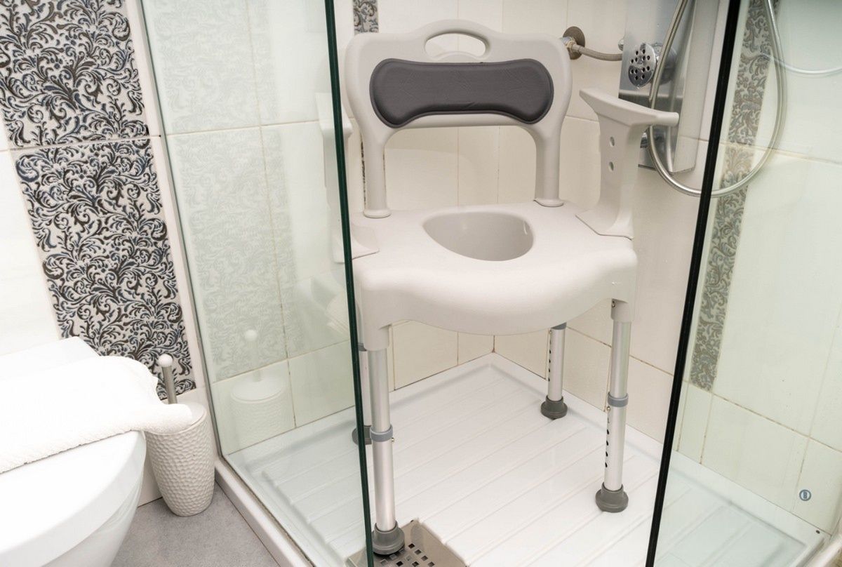 Sedia per doccia in una cabina doccia. Seduta e schienale grigi. Struttura bianca.