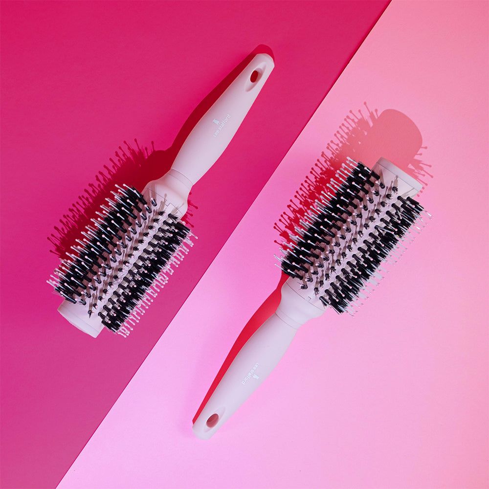Due spazzole rotonde bianche con setole nere su sfondo rosa.
