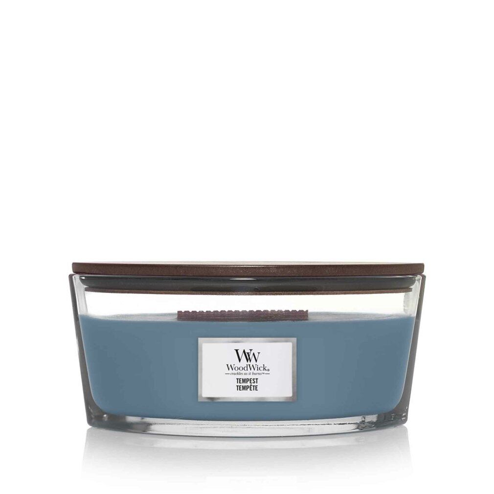 Candela blu in contenitore di vetro con coperchio in legno. Adesivo con logo e testo. Stoppino in legno visibile.