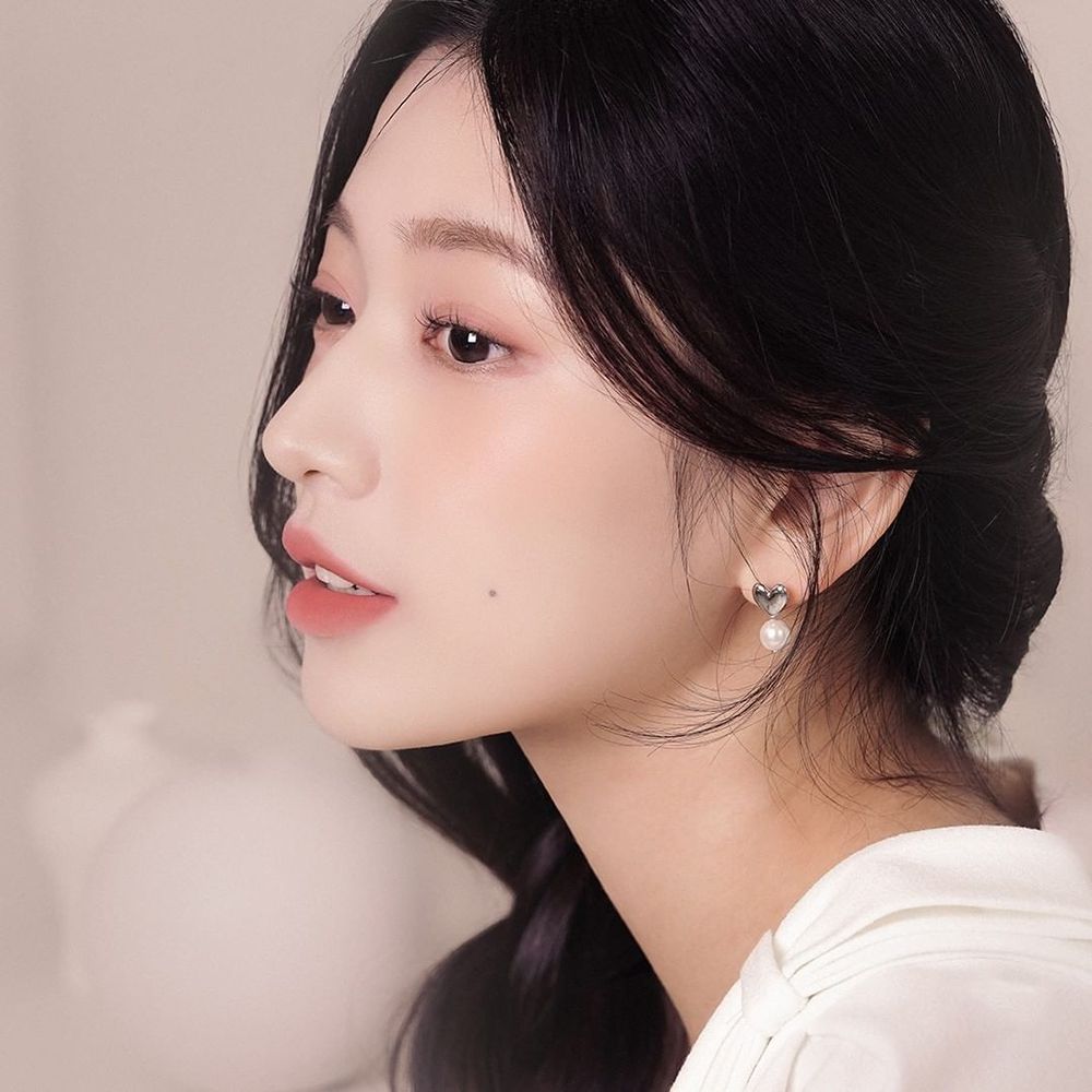 Ritratto di donna. Indossa una camicetta bianca e orecchini. I suoi capelli sono scuri e raccolti.