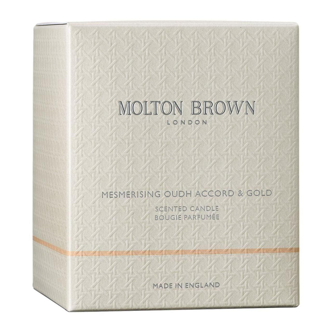 Confezione quadrata con motivo in rilievo. Scritta: Molton Brown London, Mesmerising Oudh Accord & Gold, Scented Candle, Made in England.