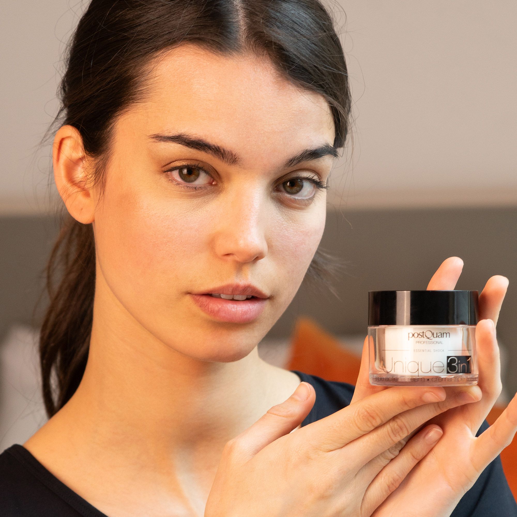 Donna che tiene in mano un vasetto di crema con coperchio nero. Scritta: Postquam Professional, Unique 3in1. Crema tripla azione.