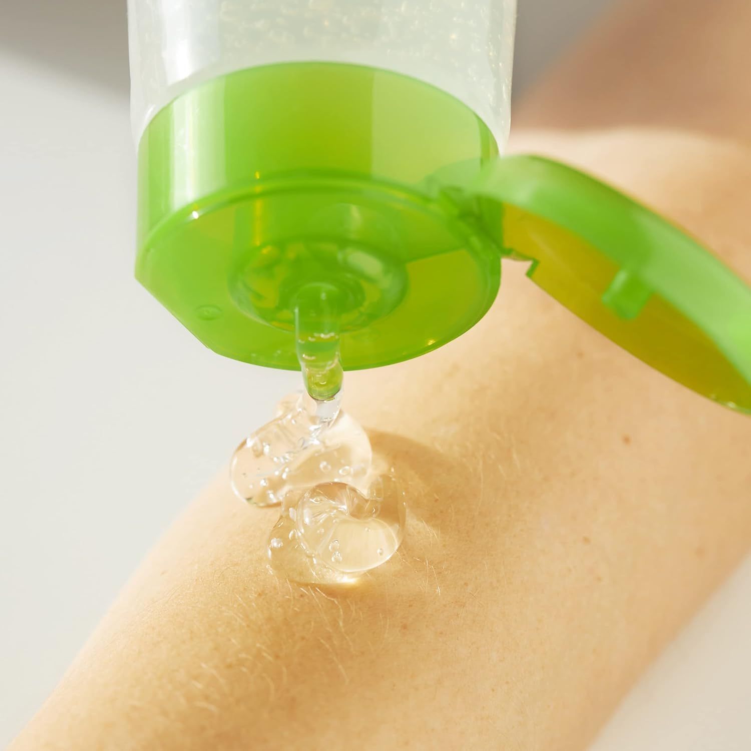 Primo piano di una mano che applica gel trasparente da un tubetto verde sulla pelle.