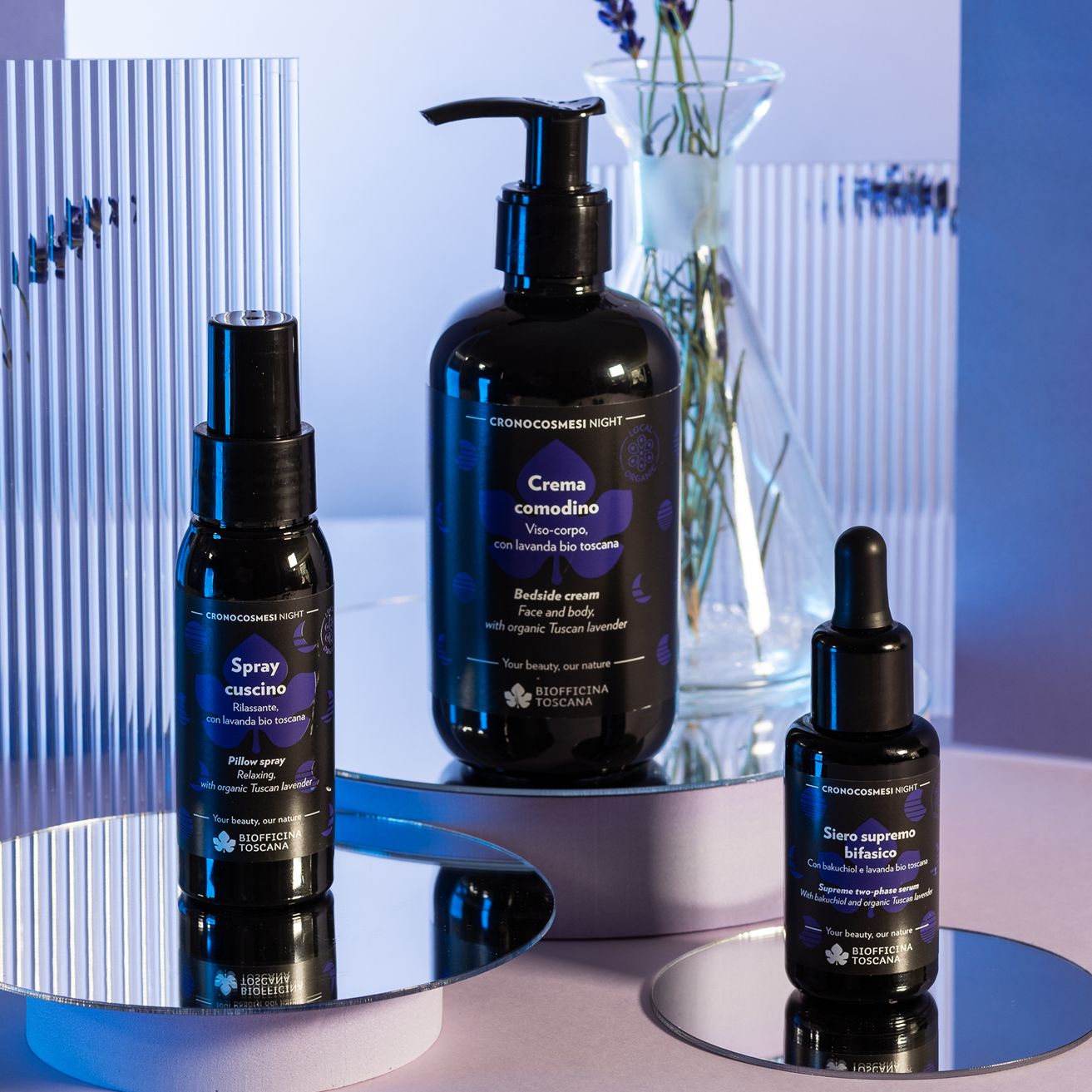 Tre flaconi neri su specchi. Scritte: Spray cuscino, Crema comodino, Siero supremo bifasico. Marchio: Biofficina Toscana.