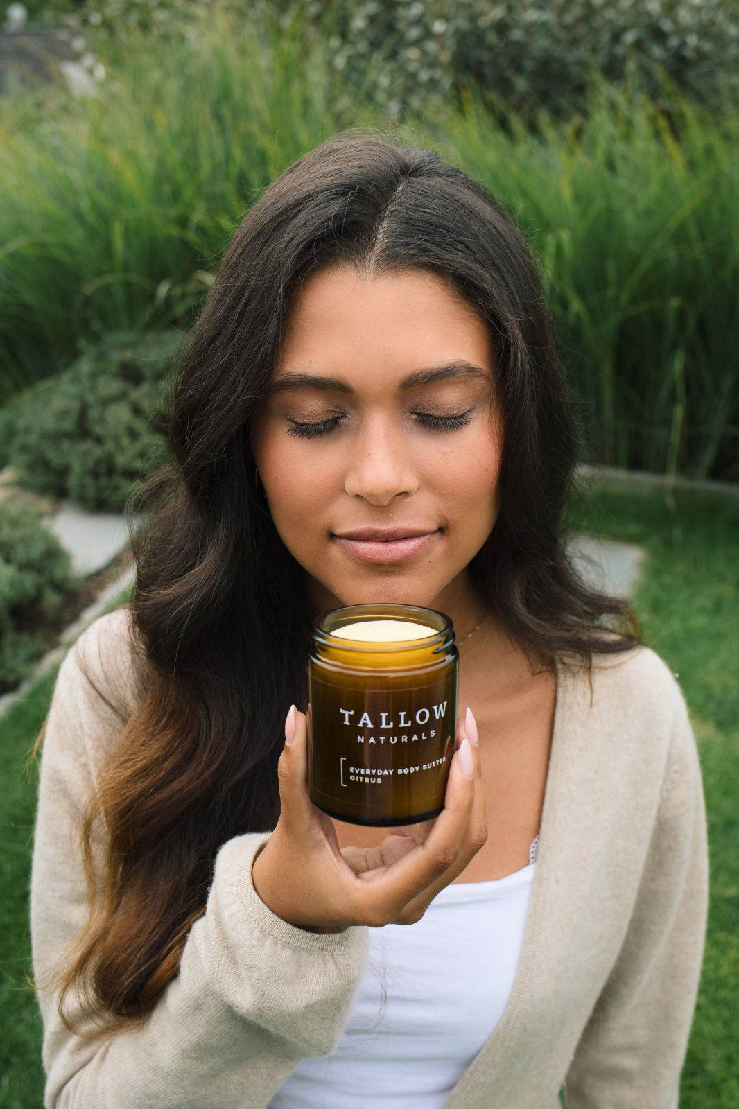 Donna che tiene un barattolo marrone con coperchio nero. Scritta: TALLOW NATURALS, EVERYDAY BODY BUTTER CITRUS. Donna chiude gli occhi.