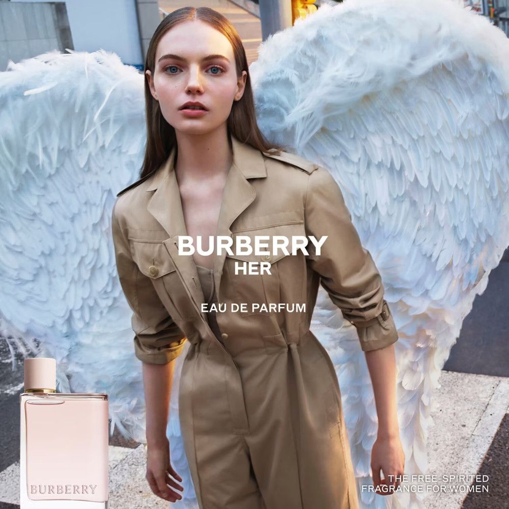 Donna con ali e flacone di Burberry Her Eau de Parfum. Scritta: Burberry Her Eau de Parfum.