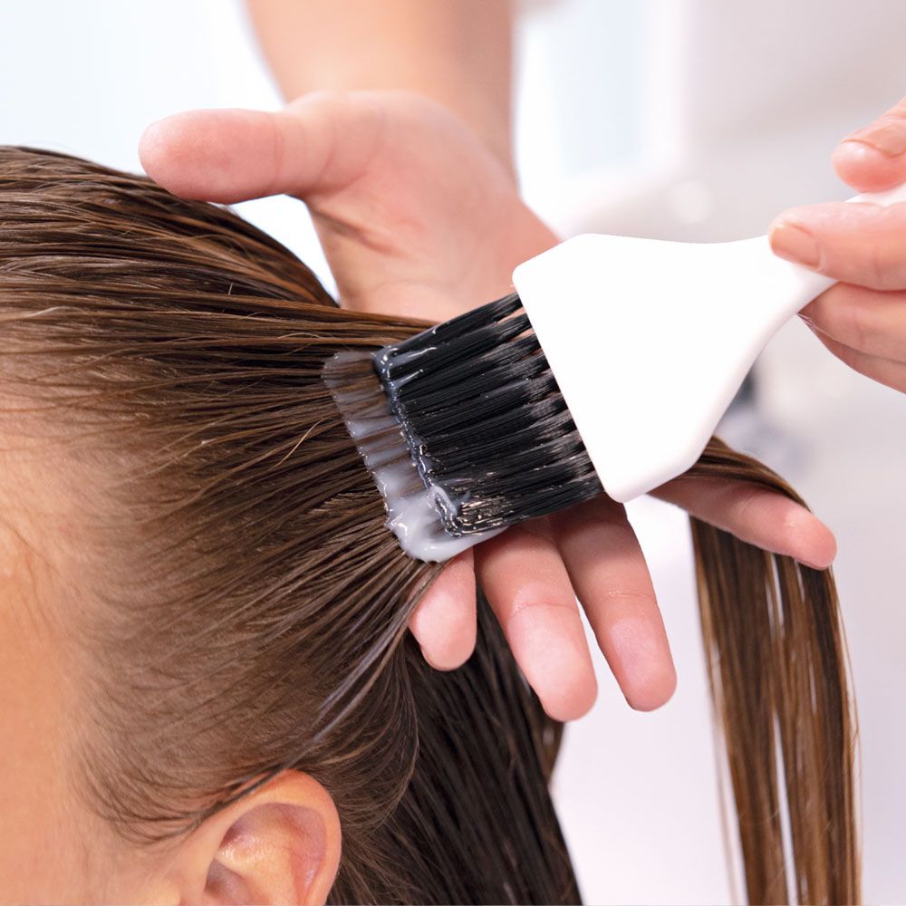 Persona applica prodotto su capelli bagnati con pennello. Setole nere, manico bianco.