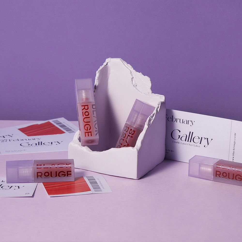 Diversi tubetti di lucidalabbra in un supporto bianco. Su sfondo viola. Scritta BLACK ROUGE.