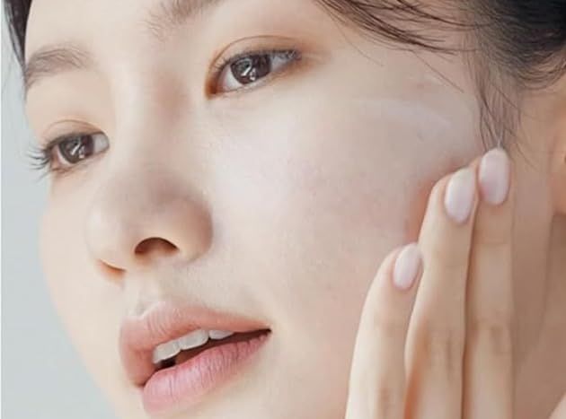 Primo piano di una donna che applica la crema solare sulla guancia.