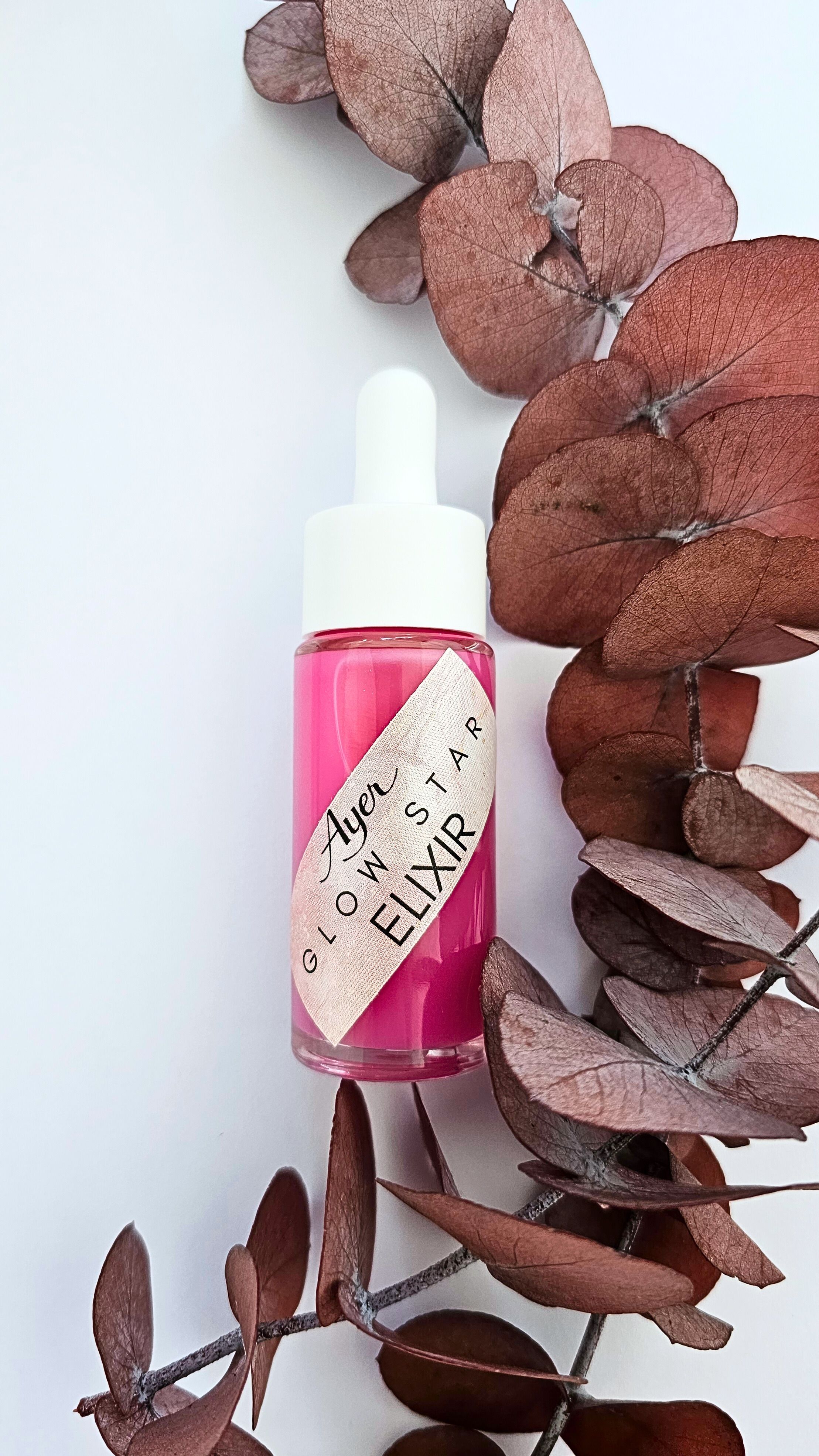 Flacone di liquido rosa con contagocce bianco, circondato da foglie secche. Etichetta: Glow Star Elixir.