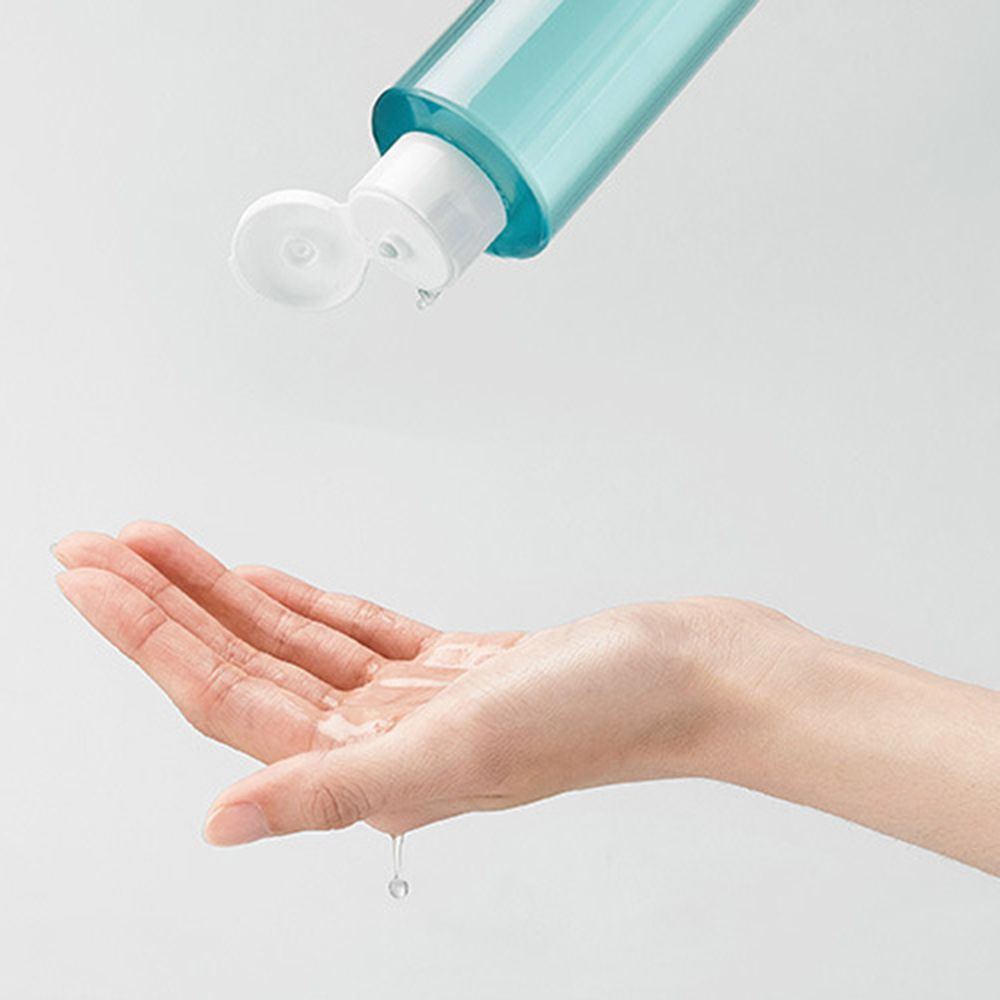 Liquido versato da un flacone in una mano. Il flacone è trasparente con contenuto blu. La mano è aperta.