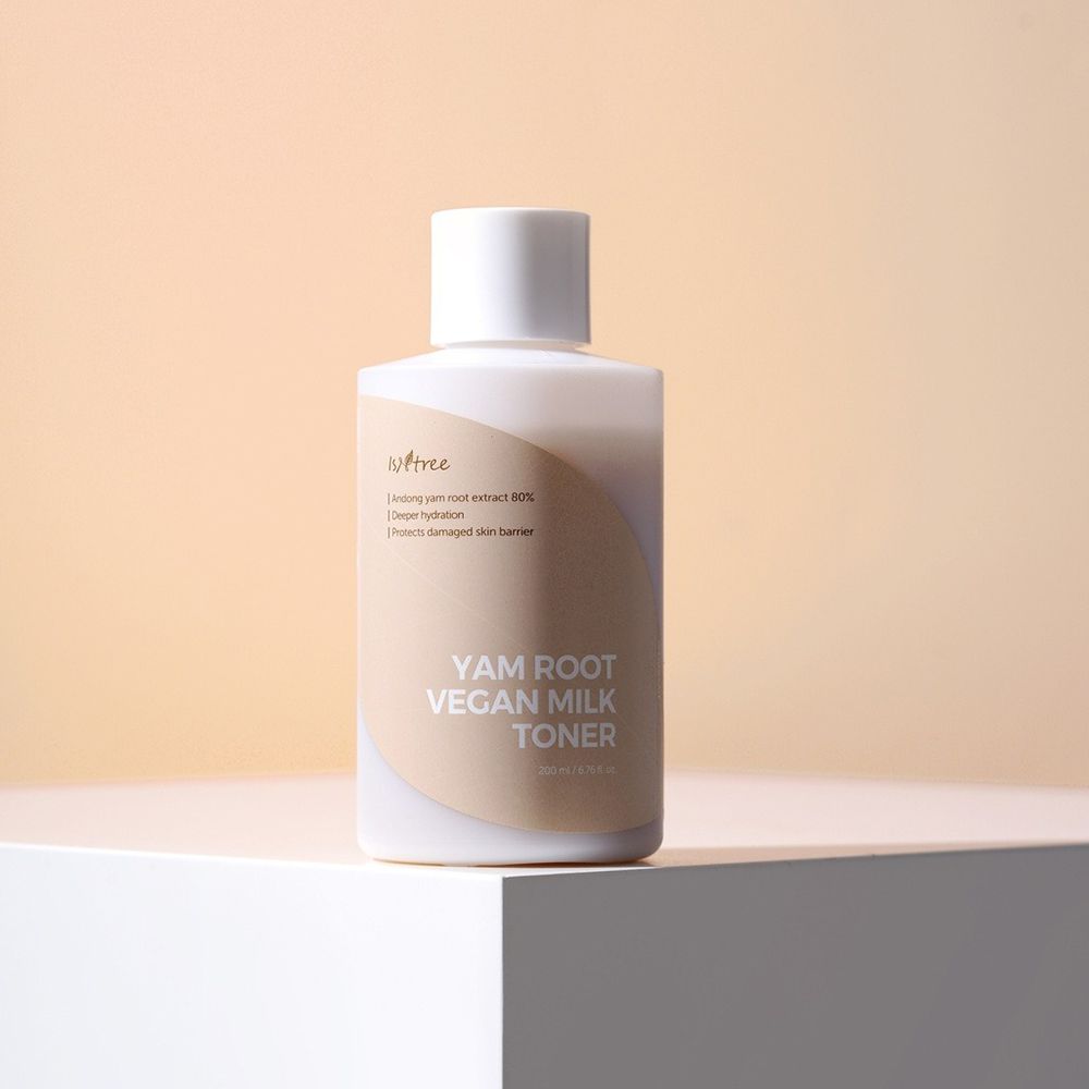 Flacone bianco con tappo bianco. Scritta: YAM ROOT VEGAN MILK TONER. Stampa beige. Su un piedistallo bianco.