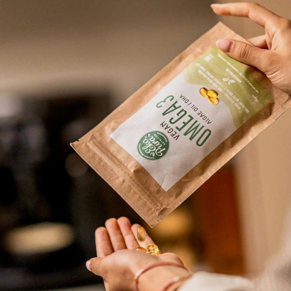 Mani che tengono una confezione marrone e capsule. Scritta: Vegan Omega 3 Algae Oil.