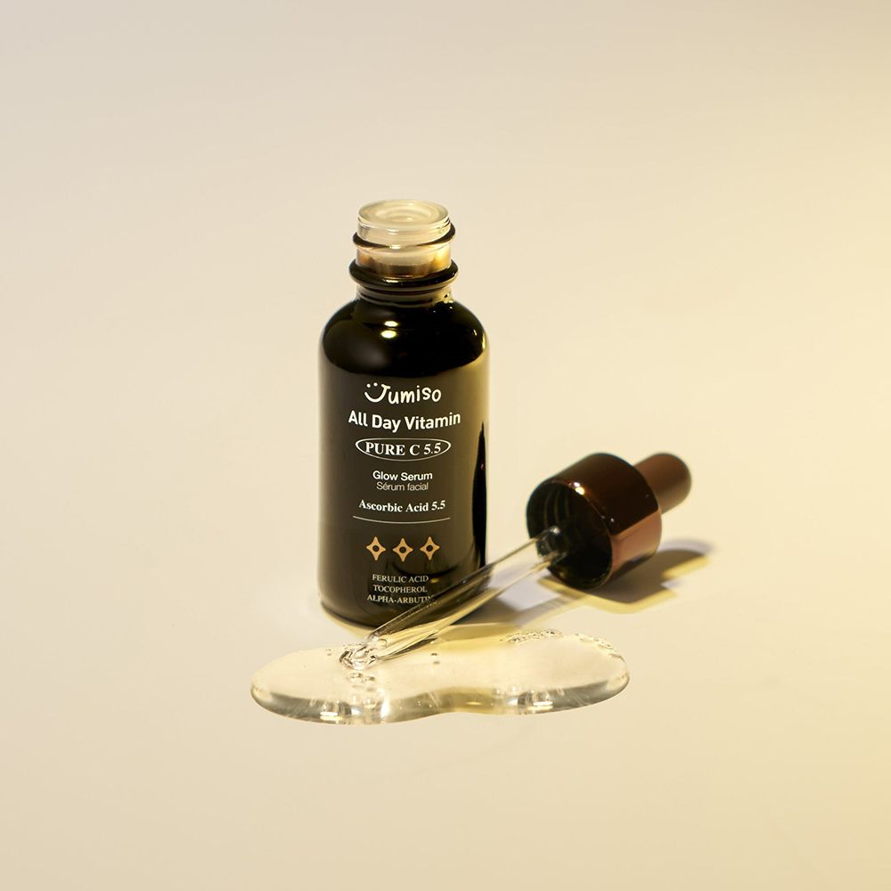 Flacone di vetro scuro con tappo e contagocce marrone. Gocce di siero accanto. Scritta: JUMISO All Day Vitamin Pure C 5.5 Glow Serum.