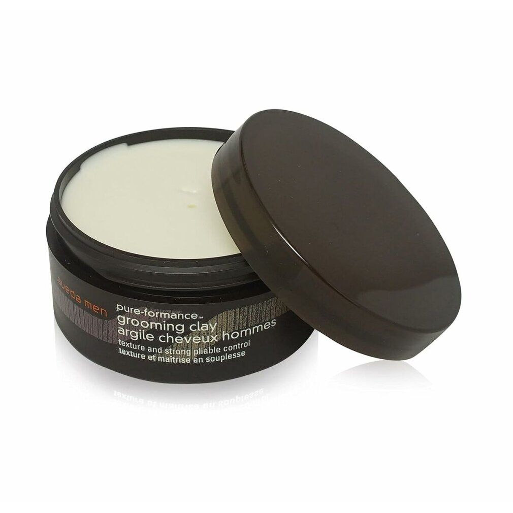 Vaso marrone scuro aperto con contenuto color crema. Coperchio accanto. Scritta: Aveda Men, pure-formance, grooming clay, argile cheveux hommes.