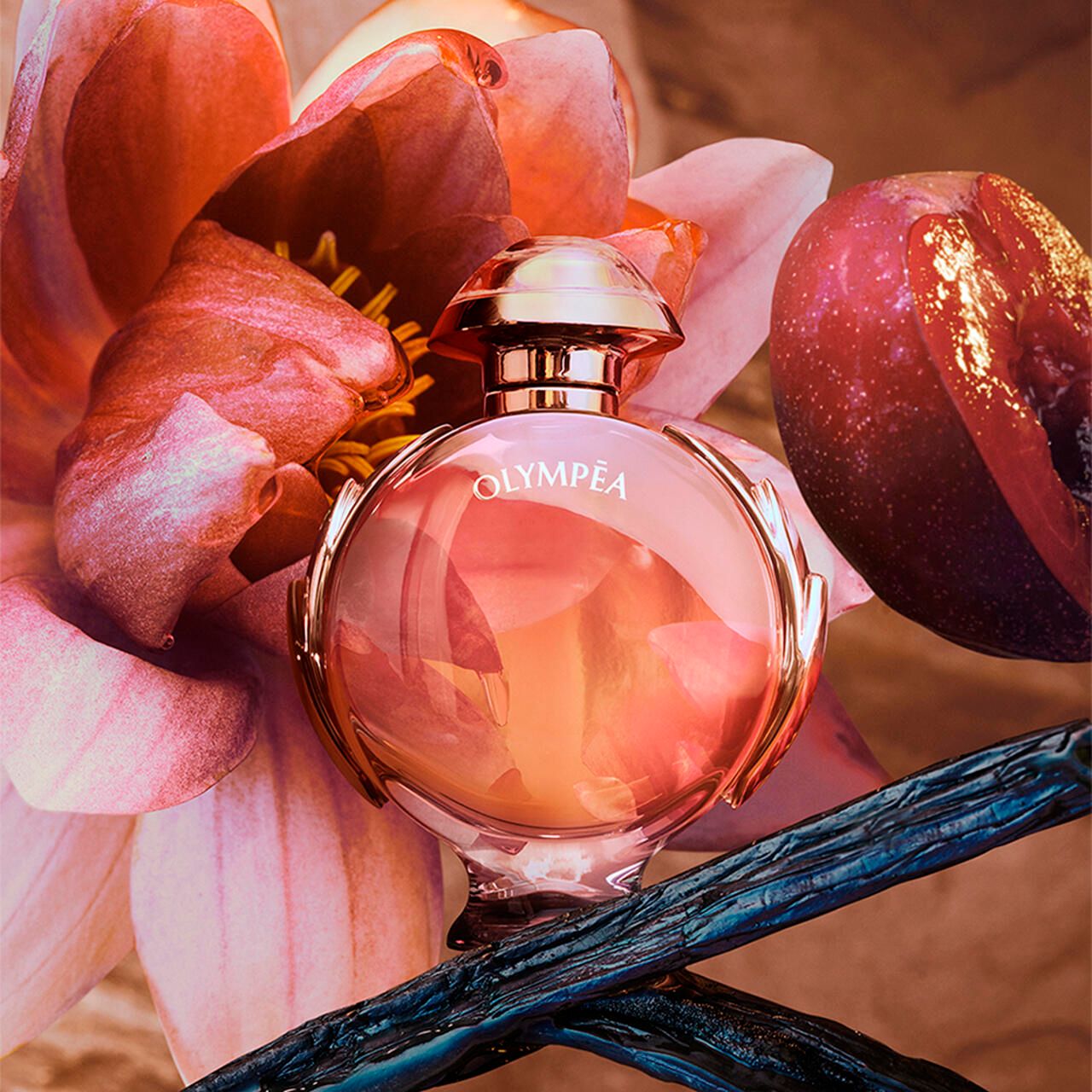 Flacone Olympéa Legend E.d.P. Nat. Spray. Sfumatura rosa, dettagli dorati. Circondato da fiori e frutta.