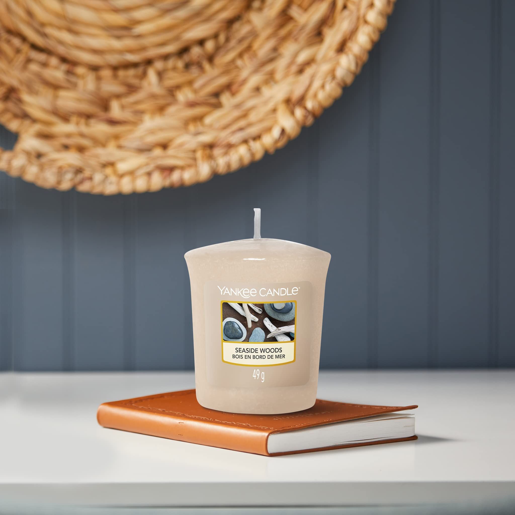 Candela beige su libro. Scritta: Yankee Candle, Seaside Woods, 49g. Cesto sullo sfondo.