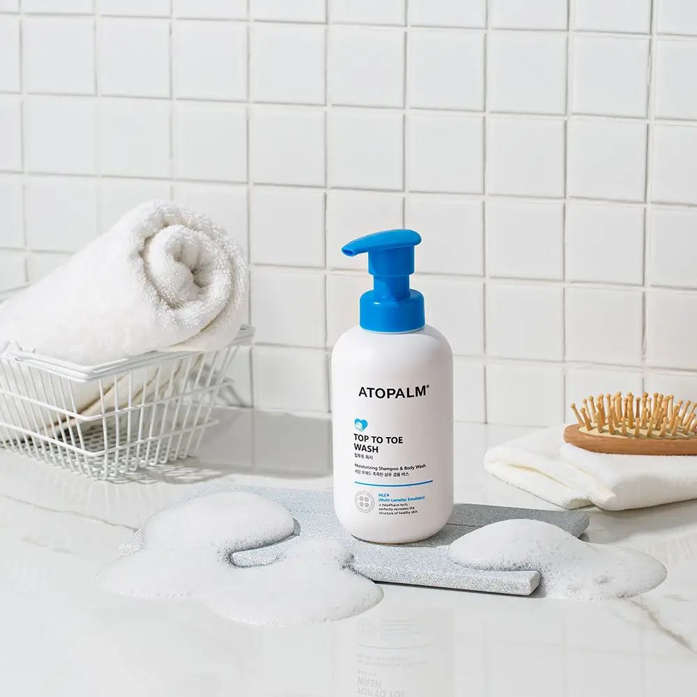 Flacone bianco con erogatore blu. Scritta: ATOPALM TOP TO TOE WASH. Schiuma, asciugamano, spazzola.
