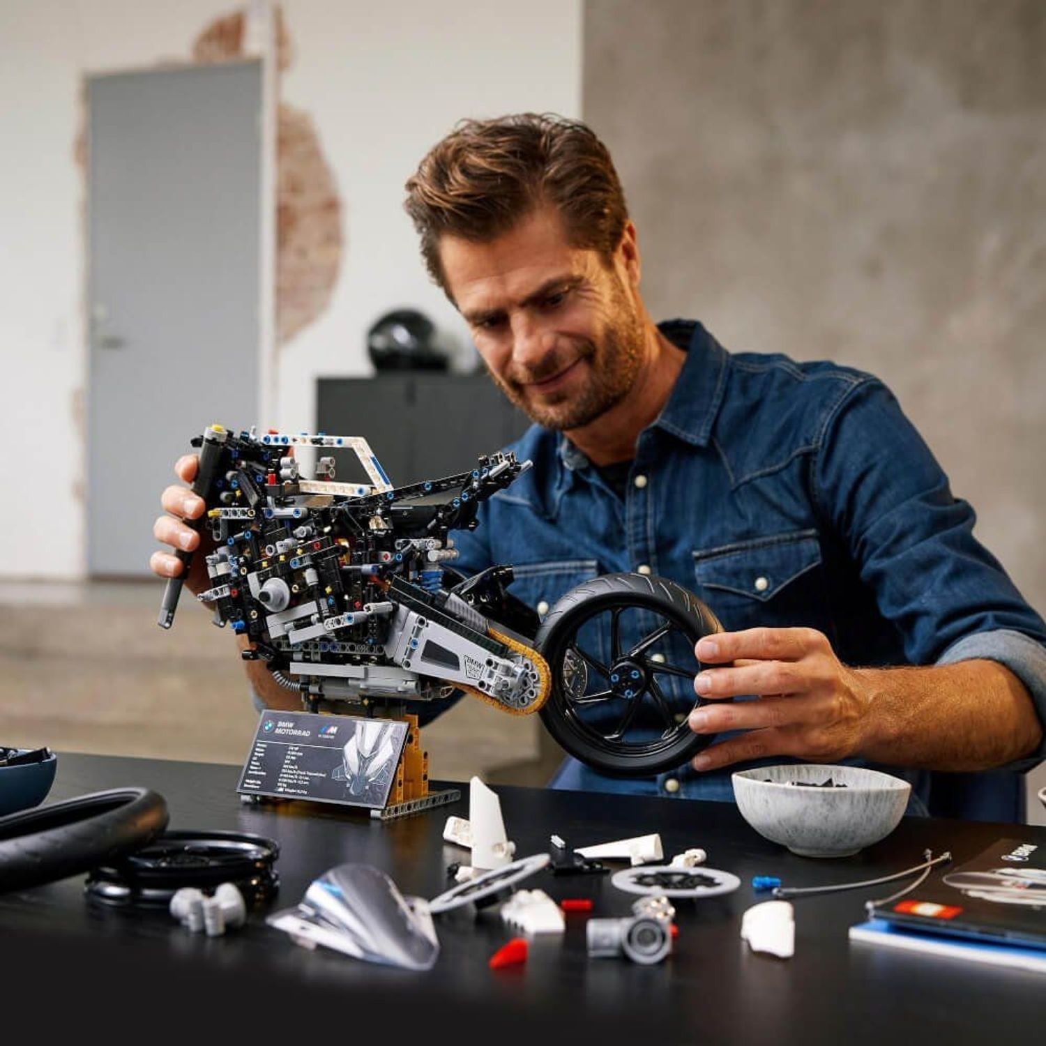 Uomo che assembla il modello moto LEGO Technic BMW M 1000 RR. Parti e accessori sul tavolo.