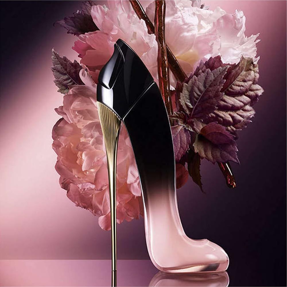 Flacone di profumo a forma di scarpa. Sfumatura nero-rosa, tacco dorato. Posizionato davanti a fiori rosa.