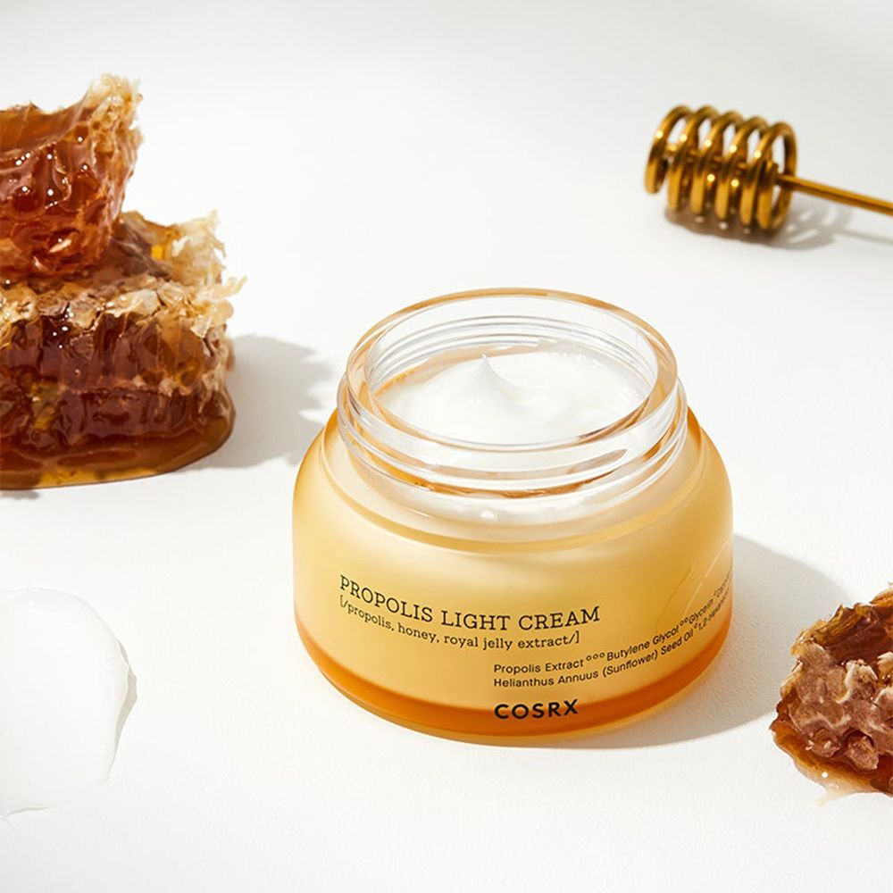 COSRX Propolis Light Cream in un barattolo di vetro con favi e mescolatore di miele.