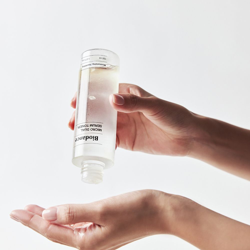 Mani che tengono un flacone di BIODANCE Micro Dual Serum Toner. Il flacone è tenuto sopra una mano. Liquido trasparente.