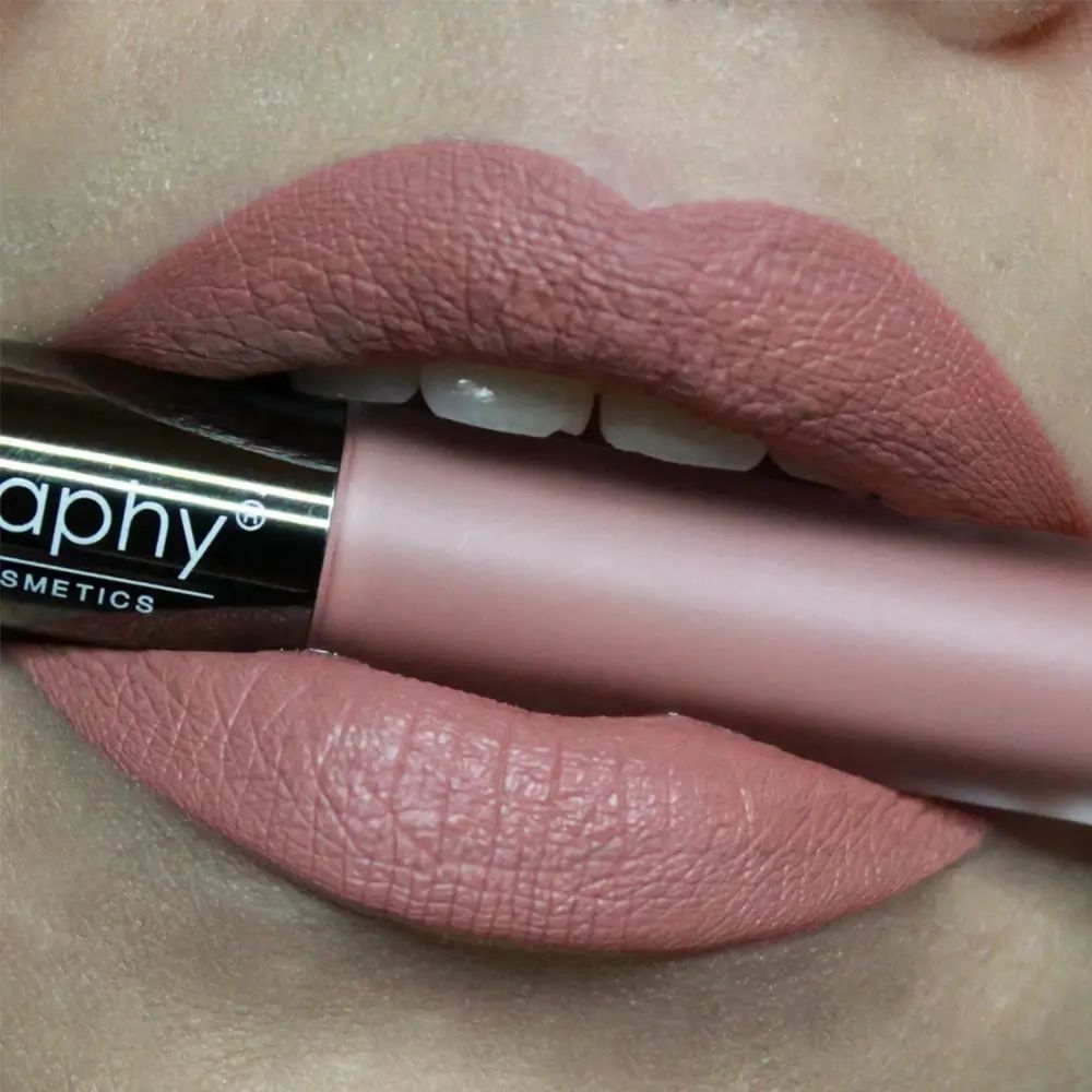 Labbra con rossetto applicato. Un applicatore di rossetto è tenuto dalle labbra. Sull'applicatore è scritto "Bodyography Cosmetics".