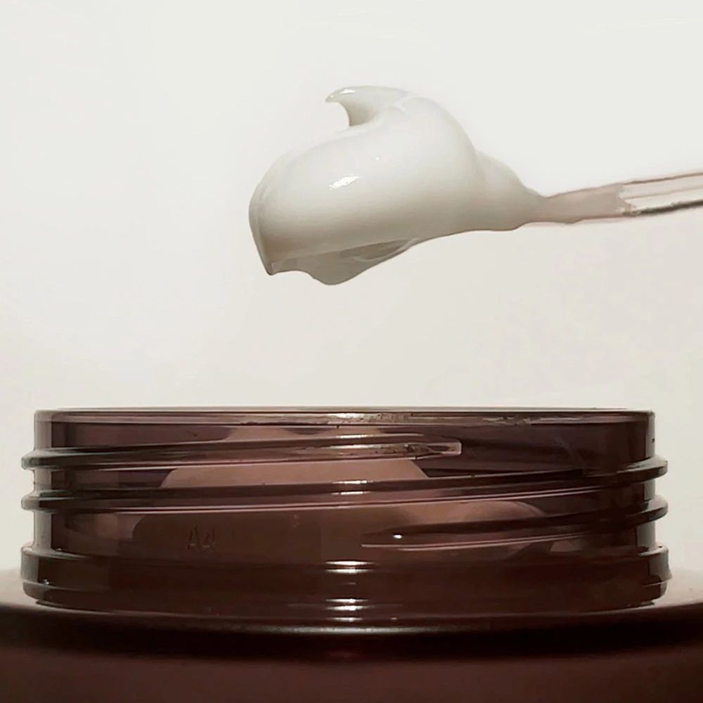 Crema su un cucchiaio. La crema è bianca e ha una consistenza liscia. Il cucchiaio è trasparente.