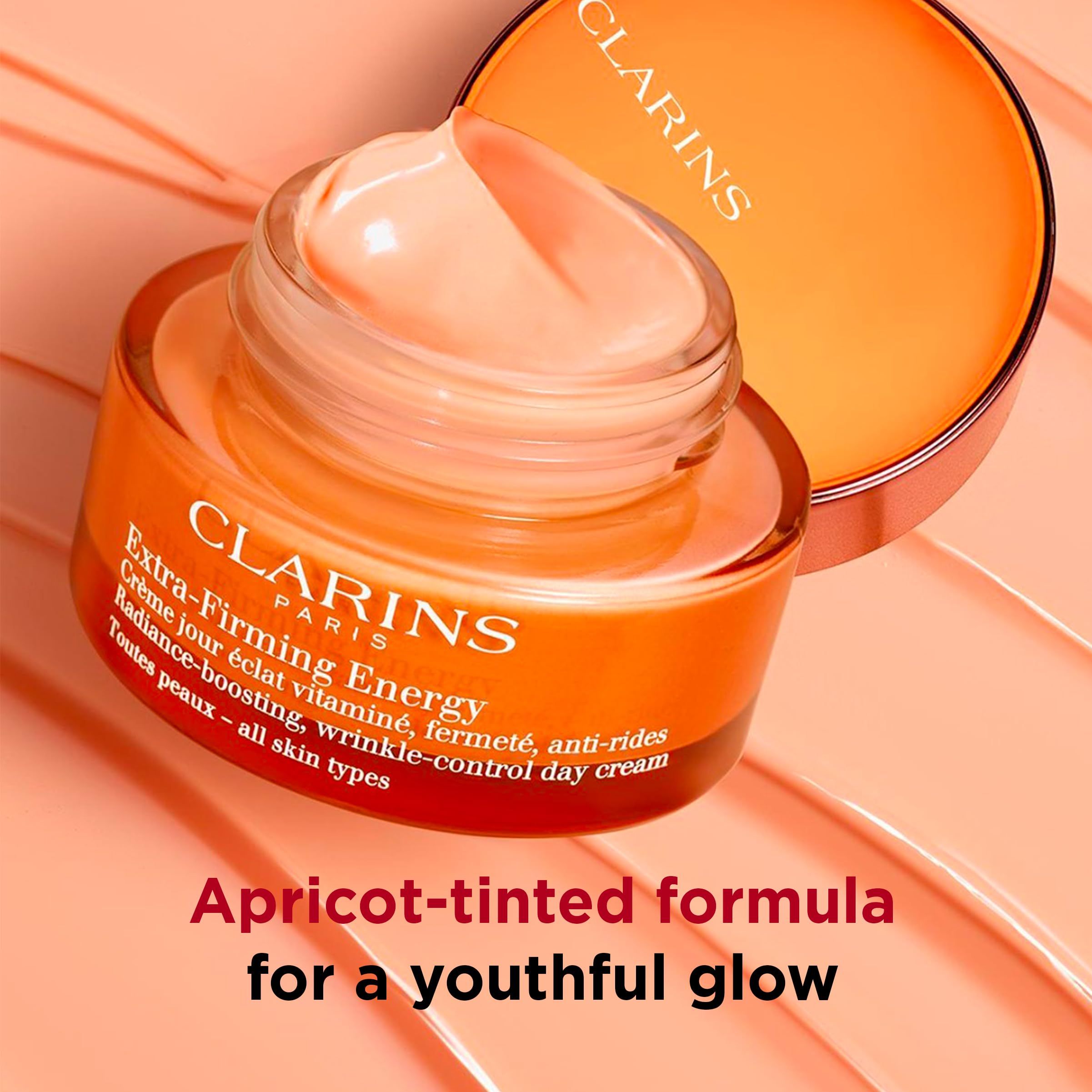 Vasetto di crema arancione con testo. Coperchio accanto. Testo: Formula color albicocca per un incarnato giovanile.