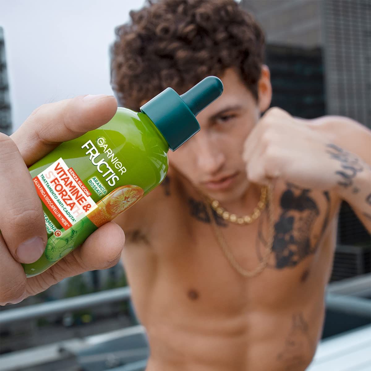 Flacone verde con contagocce, tenuto da una persona. Scritta: Garnier Fructis Vitamine & Forza. Trattamento anticaduta.