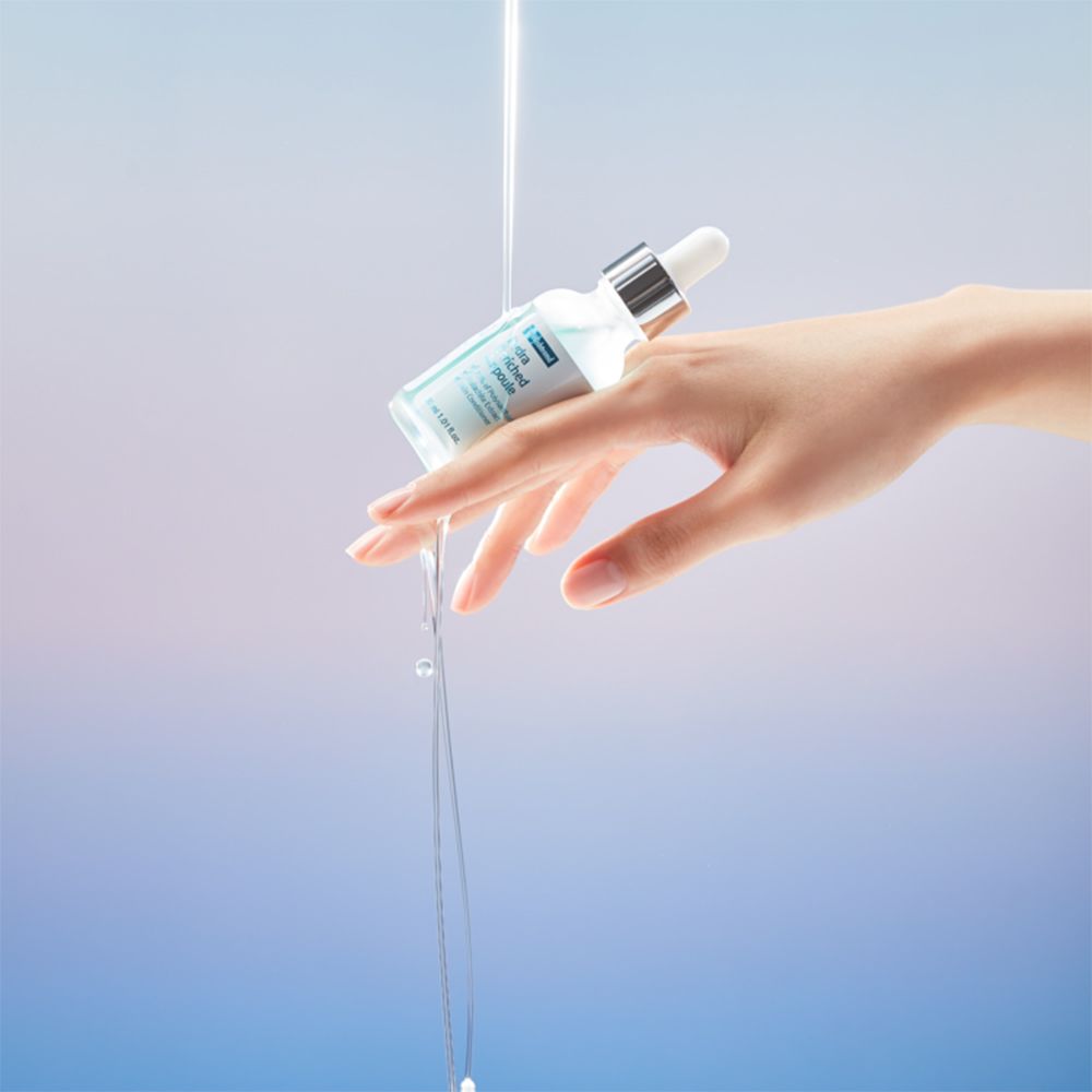 Mano che tiene un flacone di siero. Liquido che esce dal flacone. Sfondo blu e bianco.