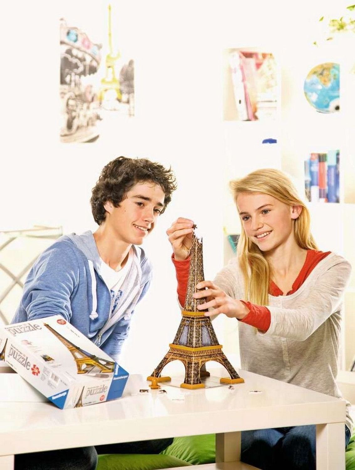 Due ragazzi assemblano un puzzle 3D Torre Eiffel. Puzzle e confezione su un tavolo. Ambiente luminoso.