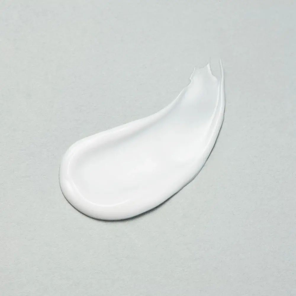 Tratto di crema bianca su sfondo grigio. Visibile la consistenza della crema.