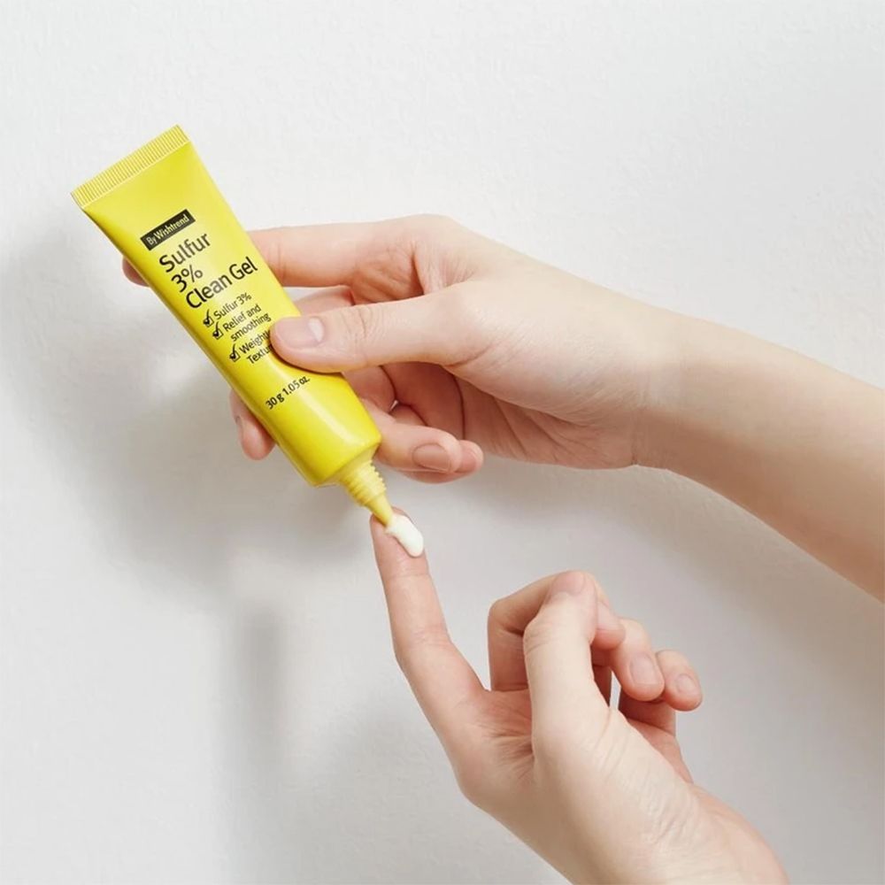 Tubo di gel giallo tenuto in mano. Il gel viene applicato su un dito. Scritta Sulfur 3% Clean Gel.