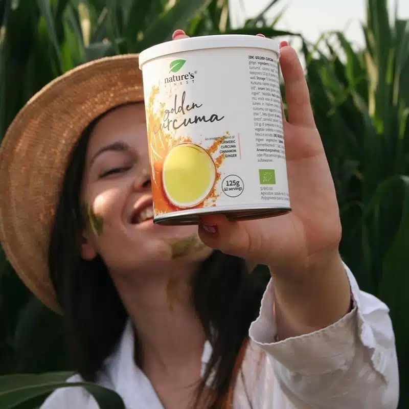 Una donna con cappello di paglia tiene una lattina di Nature's Finest Golden Curcuma Latte.