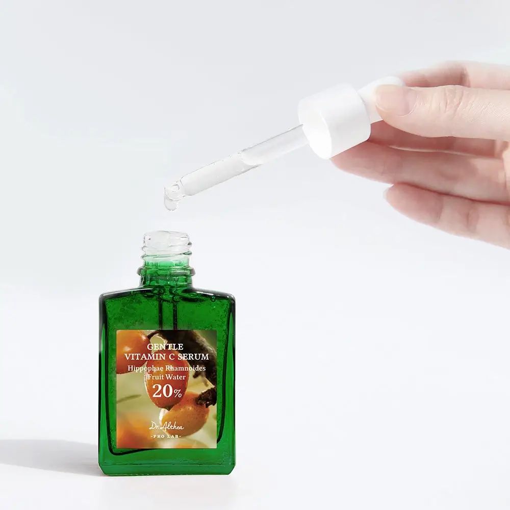 Flacone verde con contagocce. Mano che tiene il contagocce sopra il flacone aperto. Scritta: Gentle Vitamin C Serum.