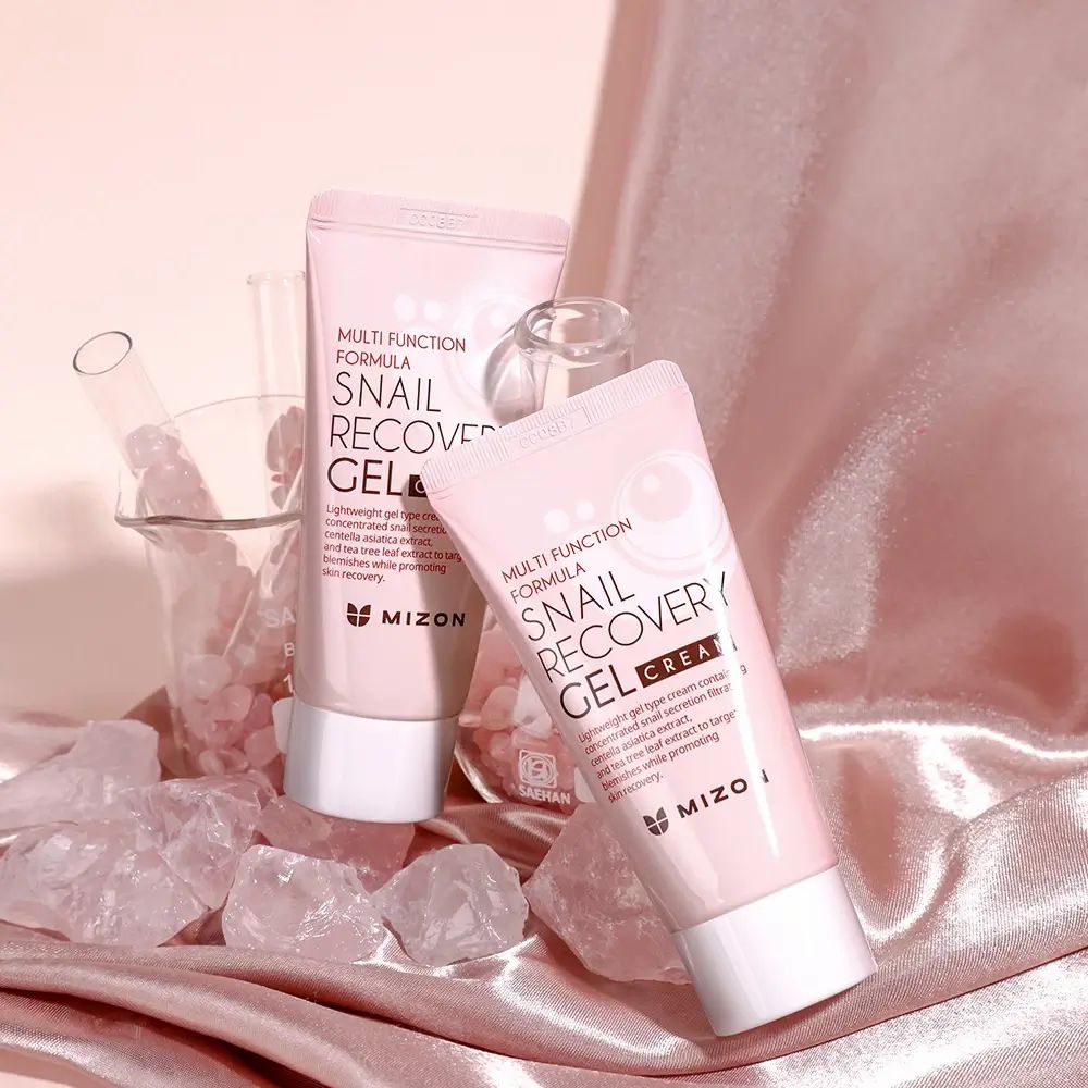 Due tubi rosa con tappo bianco. Scritta: Snail Recovery Gel Cream. Marchio: MIZON. Su tessuto rosa e pietre.