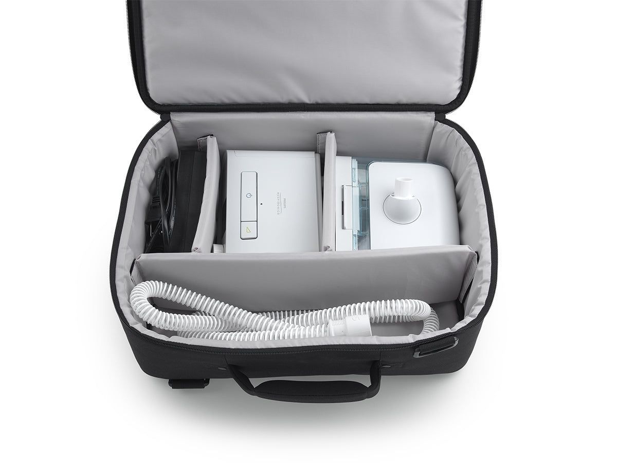 Borsa da viaggio nera, aperta, con dispositivi terapeutici bianchi e tubi all'interno, divisa in scomparti.