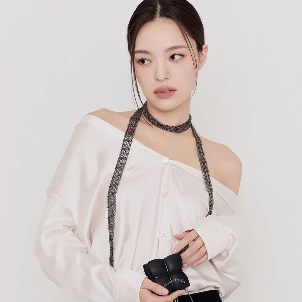 Donna con camicetta bianca e collana nera. Tiene una piccola borsa nera.