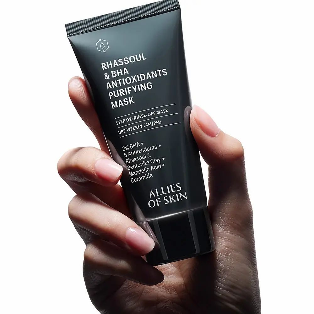 Tubo nero tenuto in mano. Nome del prodotto e ingredienti visibili. Marchio: ALLIES OF SKIN. Testo: Rhassoul & BHA Antioxidants Purifying Mask.