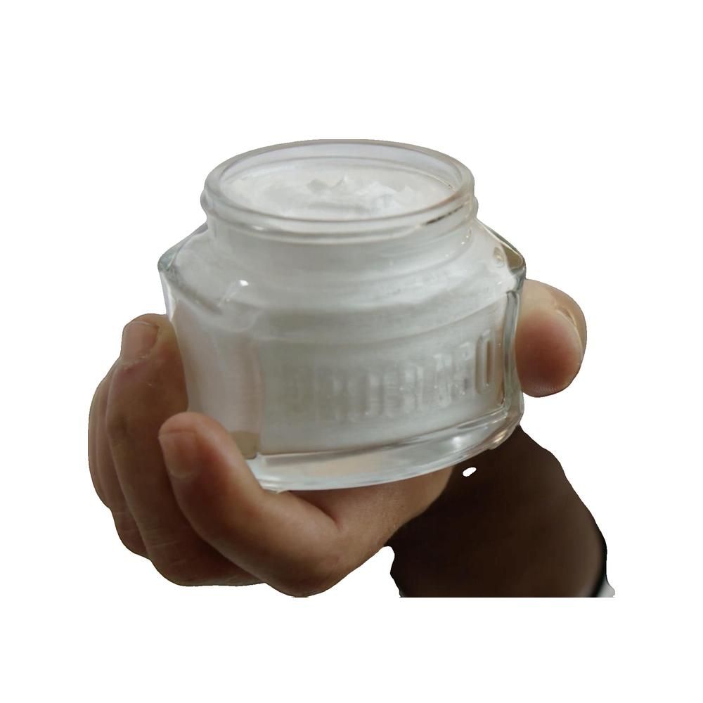 Barattolo di vetro con contenuto bianco, tenuto da una mano. Il nome del prodotto è impresso sul vetro.
