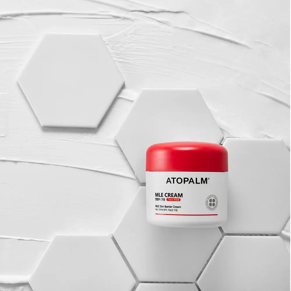 Vasetto bianco con coperchio rosso su sfondo esagonale. Scritta: ATOPALM, MLE CREAM.