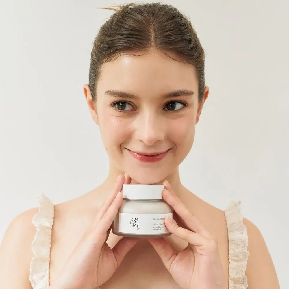 Donna che tiene il prodotto. Prodotto: Ground Rice and Honey Glow Mask. Scritta: Beauty of Joseon.
