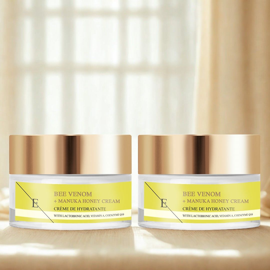 Due vasetti di crema con coperchi dorati. Etichette gialle con testo: Bee Venom + Manuka Honey Cream. Su sfondo chiaro.
